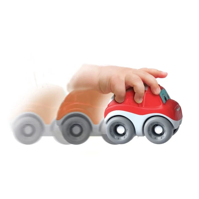 Close-up of a child's hand pushing a red Clementoni rescue car with grey wheels, white lower body and cartoon face, with a blurred image showing its movement.