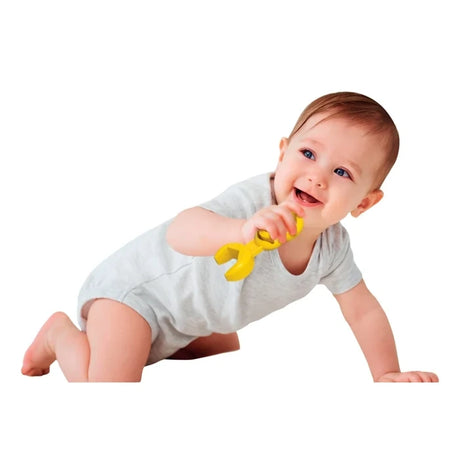 Smiling baby in a light grey outfit holding a yellow toy wrench while crawling against a white background.