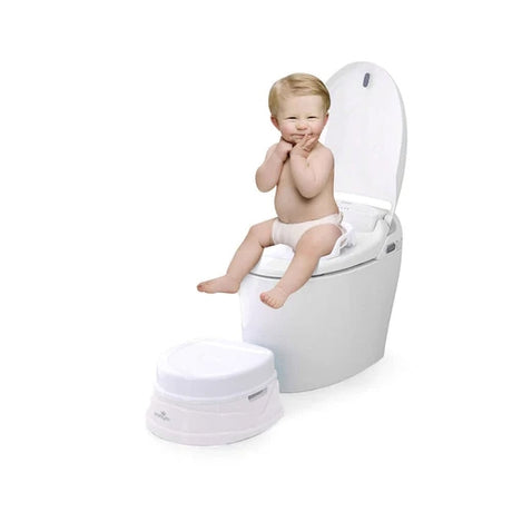Child seated on an adult toilet using the white and grey Babylo potty training seat with side handles, with the matching potty base positioned on the floor below