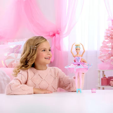 Barbie In The Nutcracker Clara Doll standing with both arms raised beside a smiling child in a pink room.