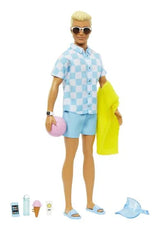 Ken doll posed for play, blue check shirt and sky blue swim shorts, towel and summer accessories arranged at his feet