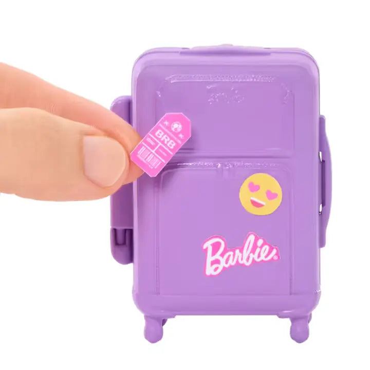 Hand adding a pink luggage tag sticker to the purple Barbie suitcase