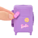 Hand adding a pink luggage tag sticker to the purple Barbie suitcase