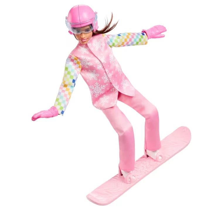 Barbie Snowboarder Doll posed balancing on a pink snowboard with both arms extended, wearing a pink helmet with goggles, pink gloves, snowflake jacket, matching trousers and white boots.