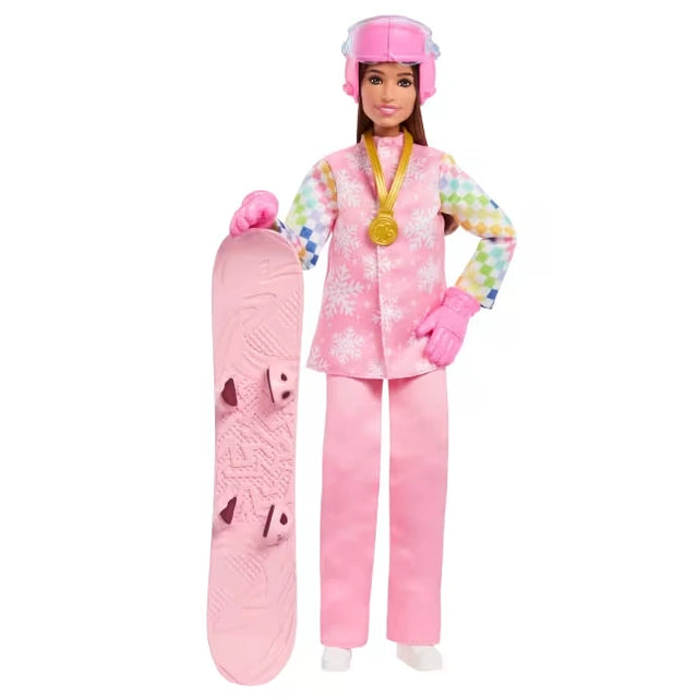 Barbie Careers Snowboarder Doll wearing a pink snowflake jacket, multicoloured checked sleeves, pink trousers, gloves and helmet, with a gold medal around her neck and a pink snowboard standing beside her.