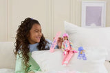 Smiling girl with curly brown hair holding a pink Barbie snowboard beside the Barbie Snowboarder Doll sitting on a white cushion, with the doll's blue hat and patterned scarf nearby.