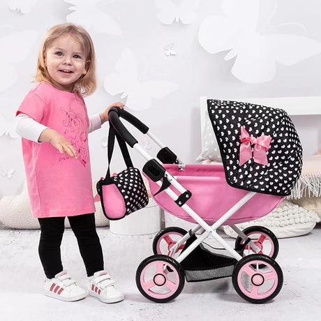 Child standing beside Bayer Design Dolls Pram Cosy pink doll pram with black polka dot hood