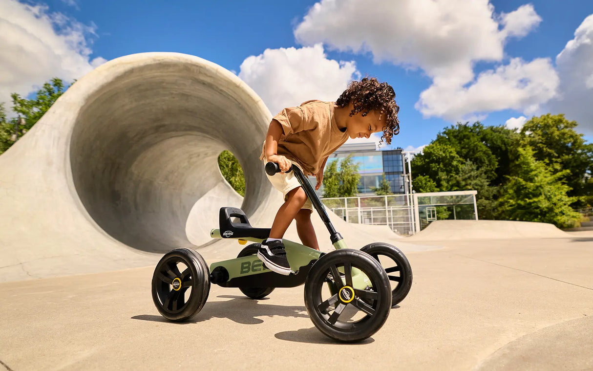 Child with BERG Buzzy Green pedal go-kart outdoors beside a large concrete tunnel