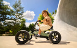 Person riding the BERG Buzzy Green pedal go-kart outdoors beside a concrete ramp