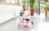 Child holding the handlebars of pink BERG GO² ride-on indoors with adult in the background