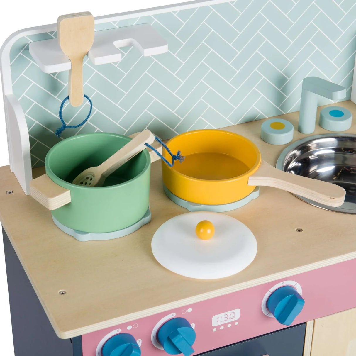 Wooden play cookware including a green pot, yellow pan, lids and utensils arranged on a wooden hob surface
