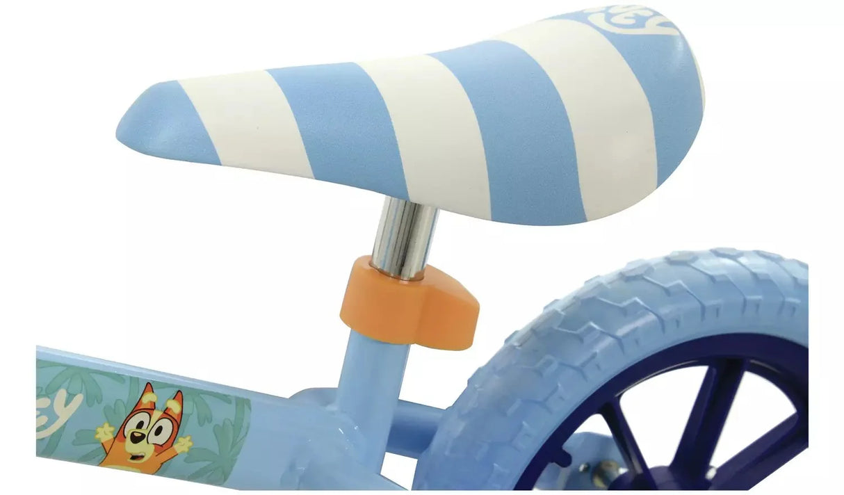 Close-up of the Bluey Light Up Balance Bike blue and white striped padded saddle on a chrome post with orange clamp, with Bingo frame graphic and rear wheel visible