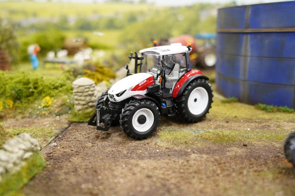 Britains Steyr 4120 Plus farm toy tractor shown side on in a model farmyard scene beside blue silos