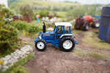Britains 1:32 Ford 8210 Tractor 43418 positioned on a model farm track with farm machinery in the background