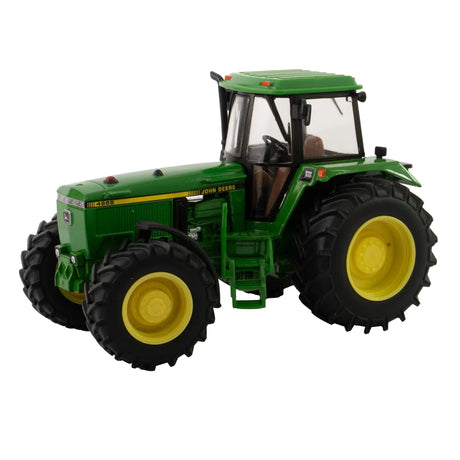 Britains John Deere 4955 tractor model shown from front left angle with green body panels, yellow wheels, large tread tyres, enclosed cab with clear windows, steering wheel and grille detail