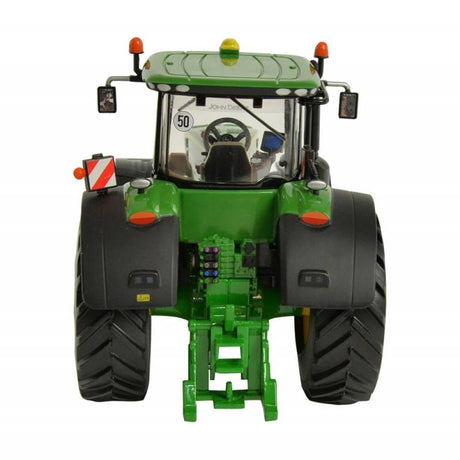 Rear view of Britains John Deere 8400R tractor model with rear hitch assembly visible, large rear tyres with deep tread, cab rear window, warning decals, and roof beacon on a white background