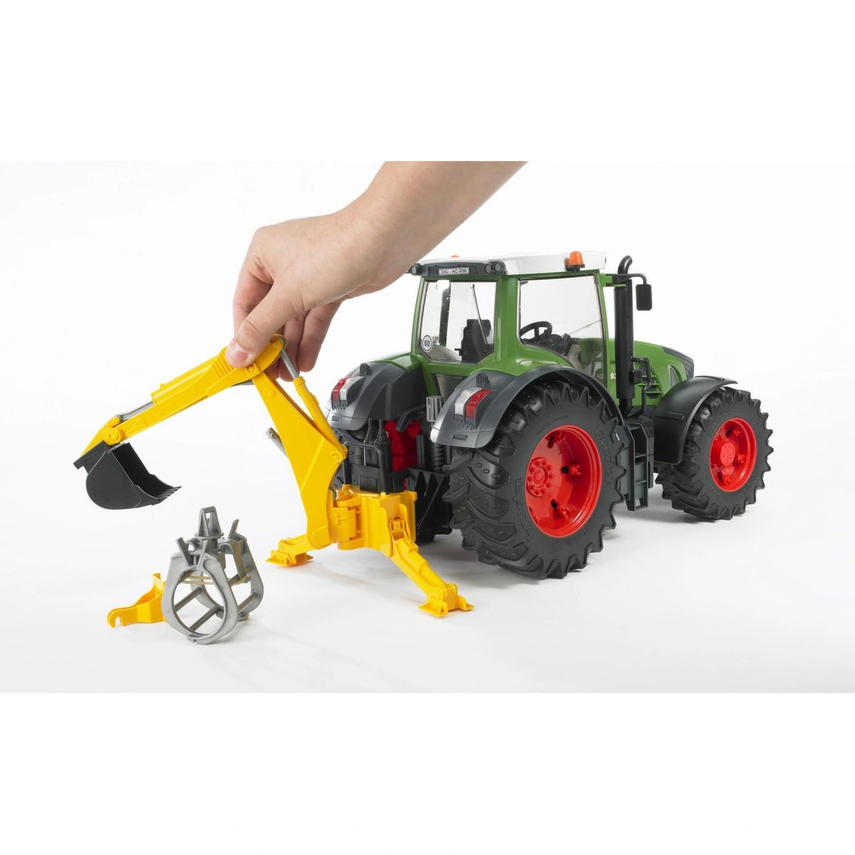 Bruder Rear Hydraulic Arm 02338 attached to a green Fendt tractor, showing a hand adjusting the yellow excavator arm with black digging bucket and separate grey grab.