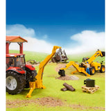 Bruder Rear Hydraulic Arm with Grab attached to a red tractor, lifting a log in a farm scene with a yellow telehandler, worker figure and construction materials.