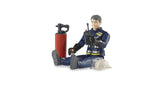 Bruder bworld Fireman 60100 seated with legs extended, holding a black radio, with the beige firefighter helmet removed and a red fire extinguisher standing beside the figure