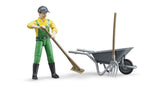bWorld farmer figure wearing green dungarees and a yellow shirt, holding a brown besom broom beside a grey wheelbarrow with a grey pitchfork on a white background.