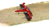 Alt: Bruder Cambridge Roller toy in red and black on a light brown ground covered with scattered straw.