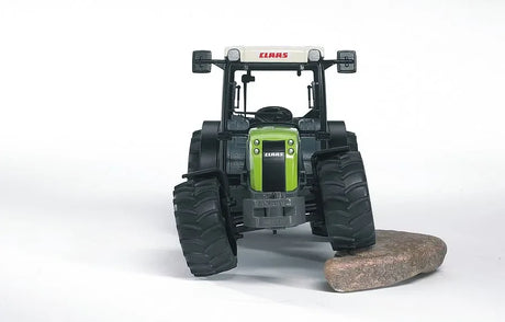 A Claas Nectis 267F toy tractor shown with its front wheels flexed as it rests on a small rock.