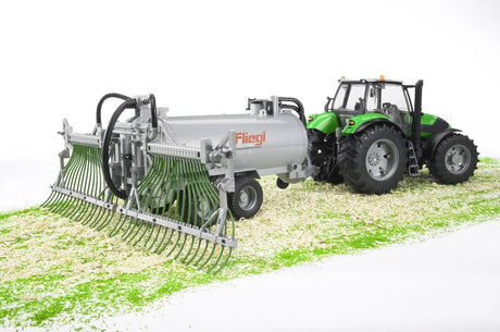 Silver Fliegl farm toy barrel trailer with green spread tubes attached to a green tractor
