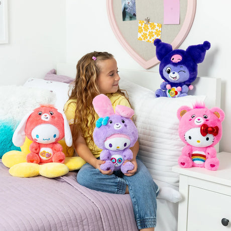 Young girl sitting on a bed holding purple My Melody as Share Bear plush, surrounded by three other Care Bears x Hello Kitty character plush toys in orange, pink and dark purple.