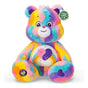 Care Bears Jumbo Plush Friends Forever Bear seated front view, showing bold multicolour striped fur, yin-yang double heart tummy badge with rainbow stripe and Caring for the Earth hang tag