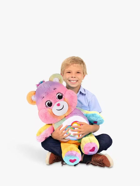 Child sitting on the floor hugging the Care Bears Jumbo Plush Togetherness Bear, showing the large size of the bear relative to a school-age child