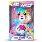 Care Bears Colours of Caring Bear medium plush in official Care Bears window box packaging, showing the full bear front-on with rainbow fur and heart tummy badge