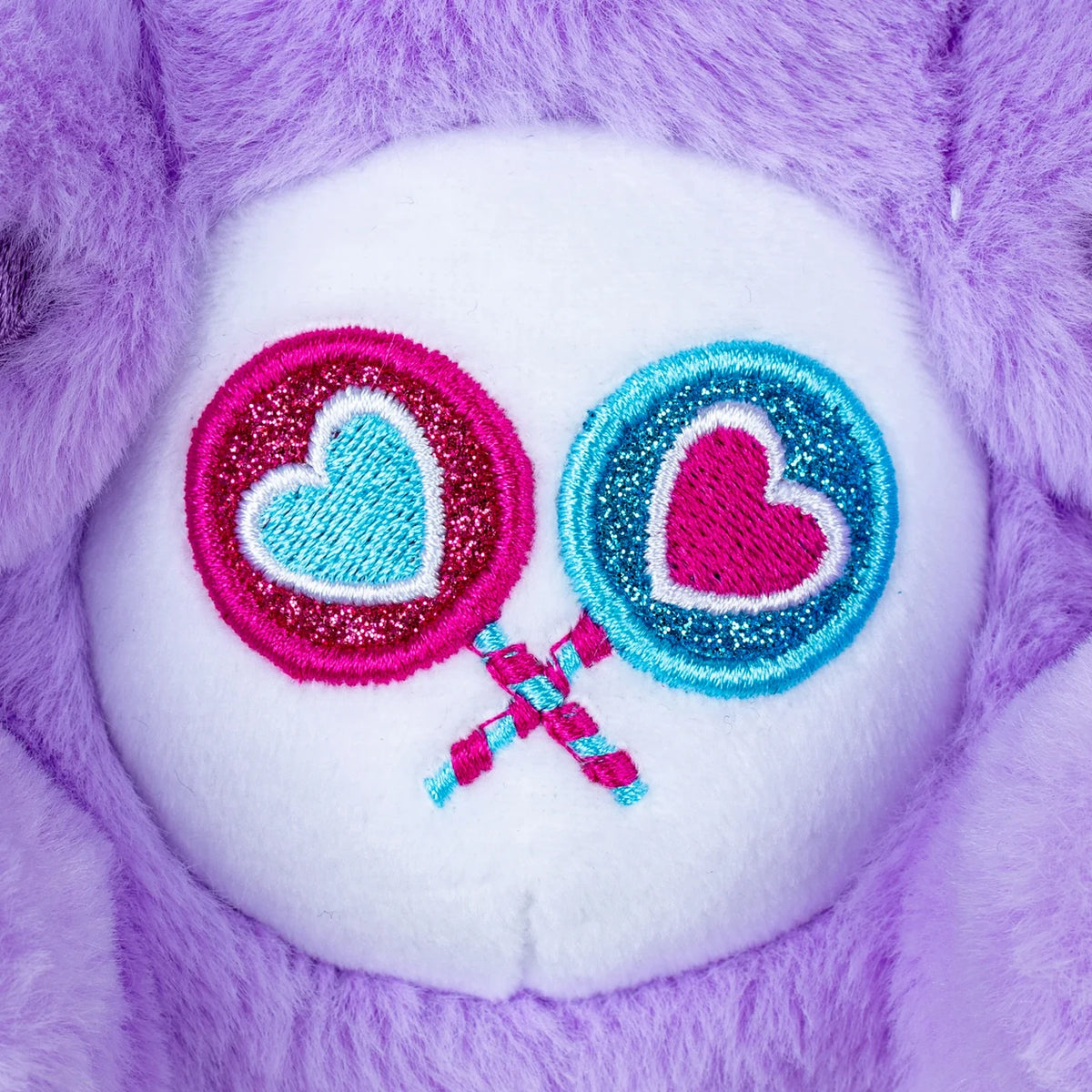 Close-up of My Melody as Share Bear's embroidered belly badge featuring two crossed heart shaped lollipops in glittery pink and turquoise stitching against white fabric.
