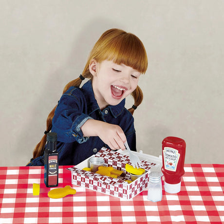 Child with open Casdon Heinz fish and chips takeaway box, ketchup bottle, vinegar bottle, salt shaker and fork
