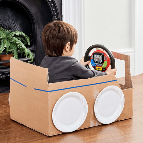 Child sitting in a cardboard car holding a Casdon Sat Nav Steering Wheel with paper plate wheels visible