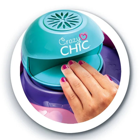 Close-up of a hand with pink painted nails placed inside the turquoise Crazy Chic nail dryer mounted on a purple base.