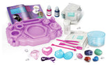 Crystal Jewellery Creator kit contents arranged on a white background, including purple workstation, instruction booklet, chemical packets, colour bottles, measuring containers, pink tools, gemstone specimens and jewellery charms.