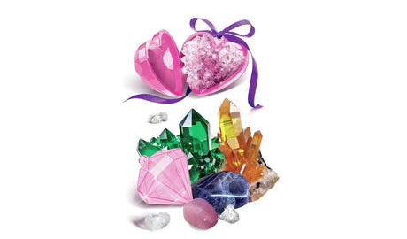 Open pink heart shaped container filled with sparkling purple crystals and tied with a purple ribbon, displayed above green and amber crystal clusters, colourful gemstones and a pink diamond shaped pendant.