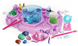 Purple Crystal Jewellery Creator workstation with a transparent blue cup containing crystals, green and yellow crystal clusters, pink tweezers, coloured stones and a pink heart shaped jewellery container.