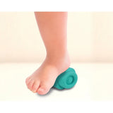Close-up of a baby's bare foot pressing down on a turquoise Soft Clemmy block, showing the block compressed beneath the foot.