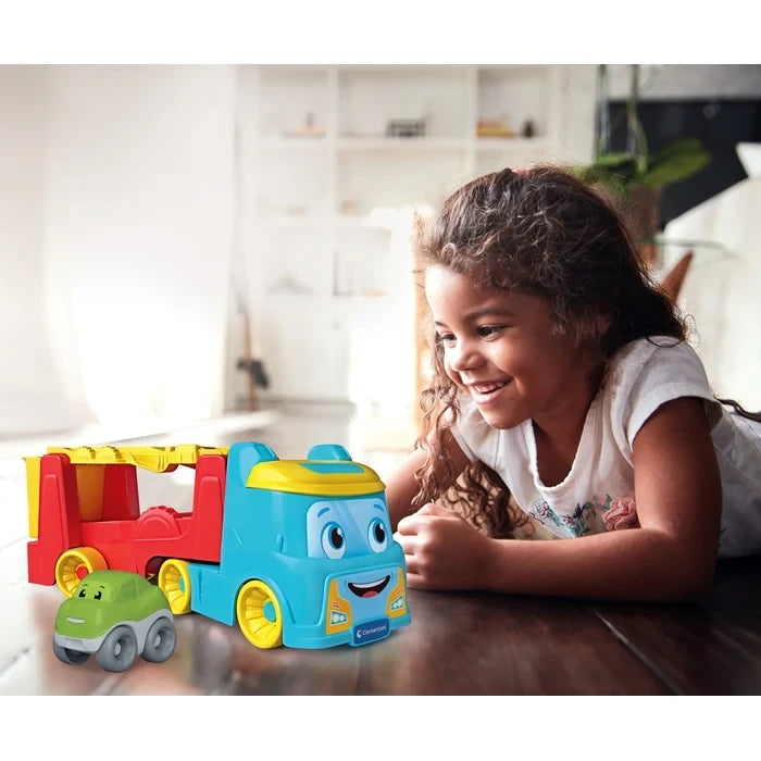 Young girl lying on a wooden floor beside the blue and red Clementoni Tumbling Car Transporter and its green tumbling car.