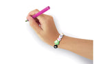 Close-up of a hand holding a pink decorating tool while wearing a bracelet made with white letter beads spelling ZOE, a green star bead and a black letter bead.