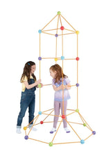 Two girls standing inside a tall pointed Crazy Forts structure built with orange rods and multicoloured connector balls.