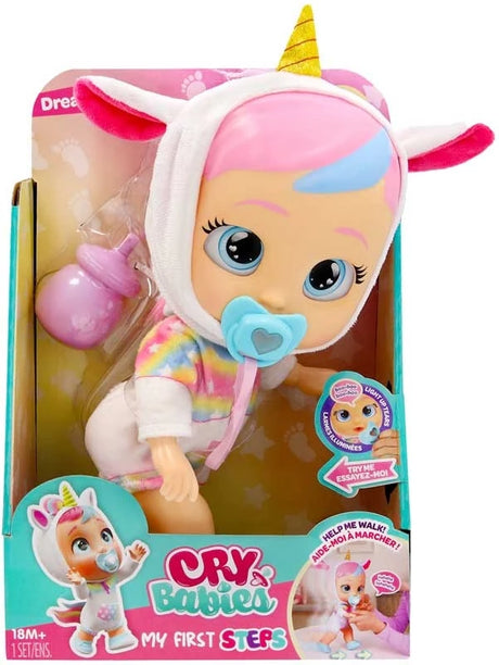 Cry Babies My First Steps Dreamy in retail packaging, wearing a white unicorn hood with pink ears and a yellow horn, with a turquoise dummy in her mouth and pink feeding bottle beside her.