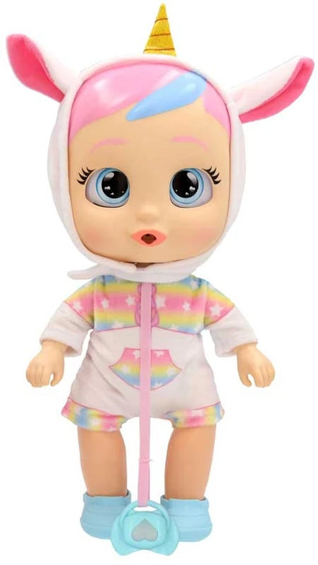Front view of Cry Babies My First Steps Dreamy standing in a white unicorn outfit with pink ears, yellow horn, rainbow sleeves and shorts, turquoise shoes and matching dummy hanging from a pink ribbon.