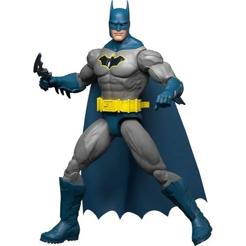 DC Batman blue and grey action figure in a wide stance with a flowing blue cape, yellow utility belt, blue mask and boots, holding a black Batarang against a white background.