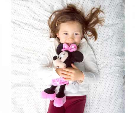 Smiling child lying on a bed hugging a Minnie Mouse plush toy dressed in pink polka dots