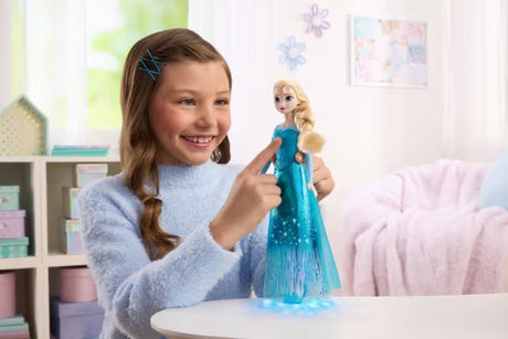 Disney Frozen Light-Up Singing Elsa Doll held by a child with blue light patterns visible on the table.