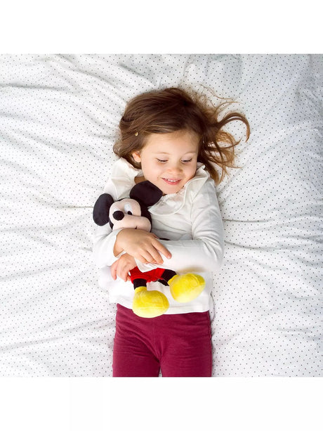 Young child lying on a bed hugging a Disney Mickey Mouse plush soft toy, showing the toy's size relative to a small child