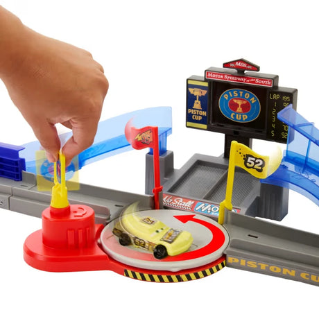 Close up of Disney Pixar Cars playset with hand pressing yellow launcher beside a yellow race car