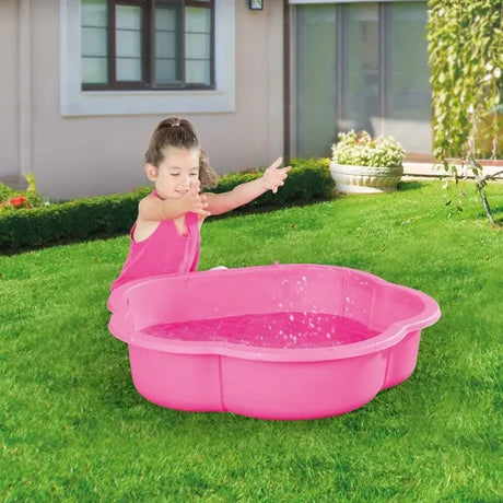 Child standing beside a pink shell shaped pool filled with water on grass